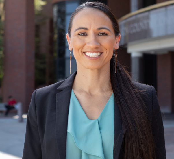 A woman wearing a black jacket and a blue shirt smiles for the camera