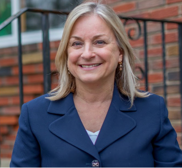 A woman in a blue jacket is smiling in front of a brick building