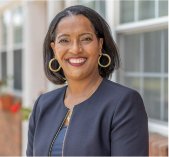 A woman wearing a black jacket and gold hoop earrings is smiling for the camera.