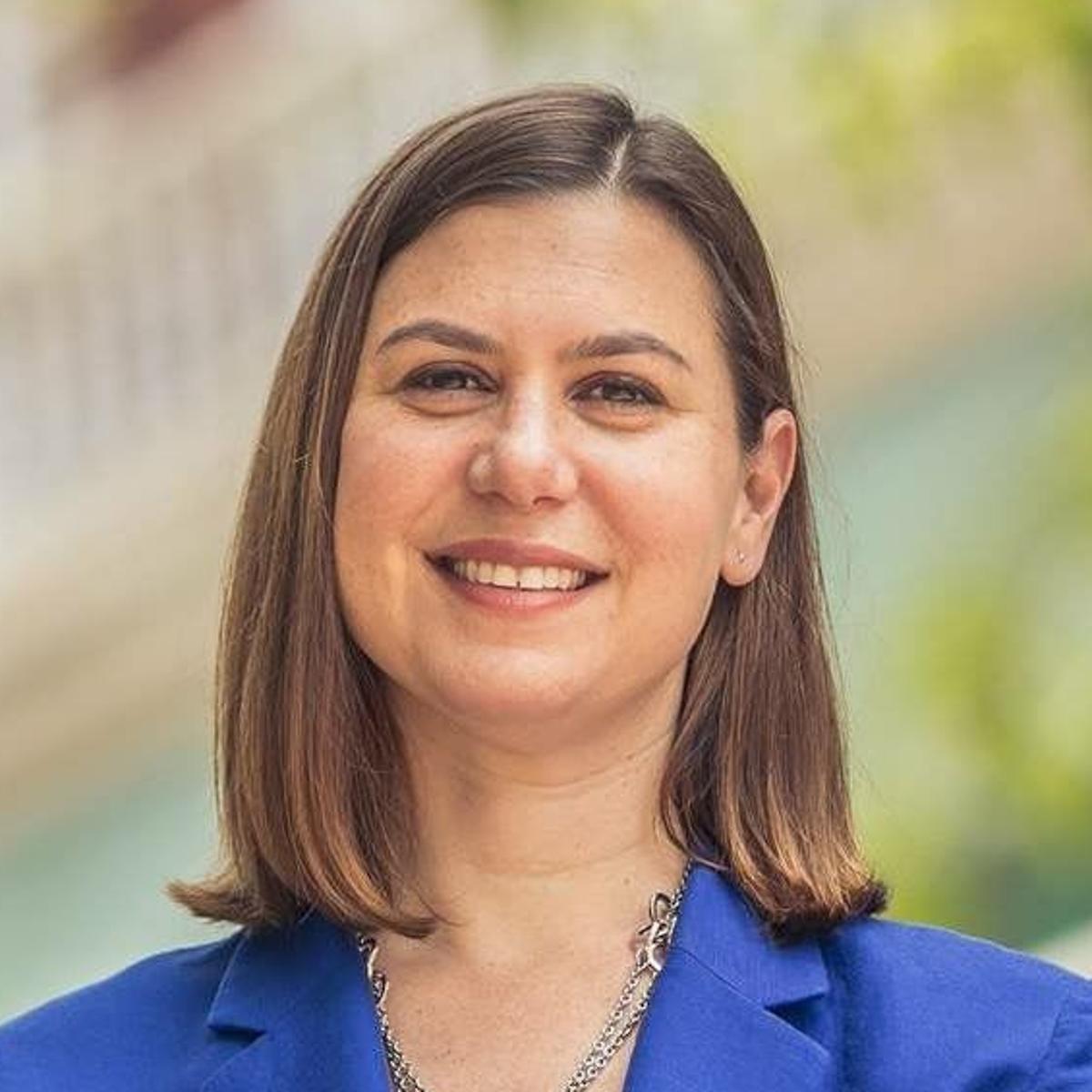 A woman in a blue jacket and necklace is smiling for the camera.