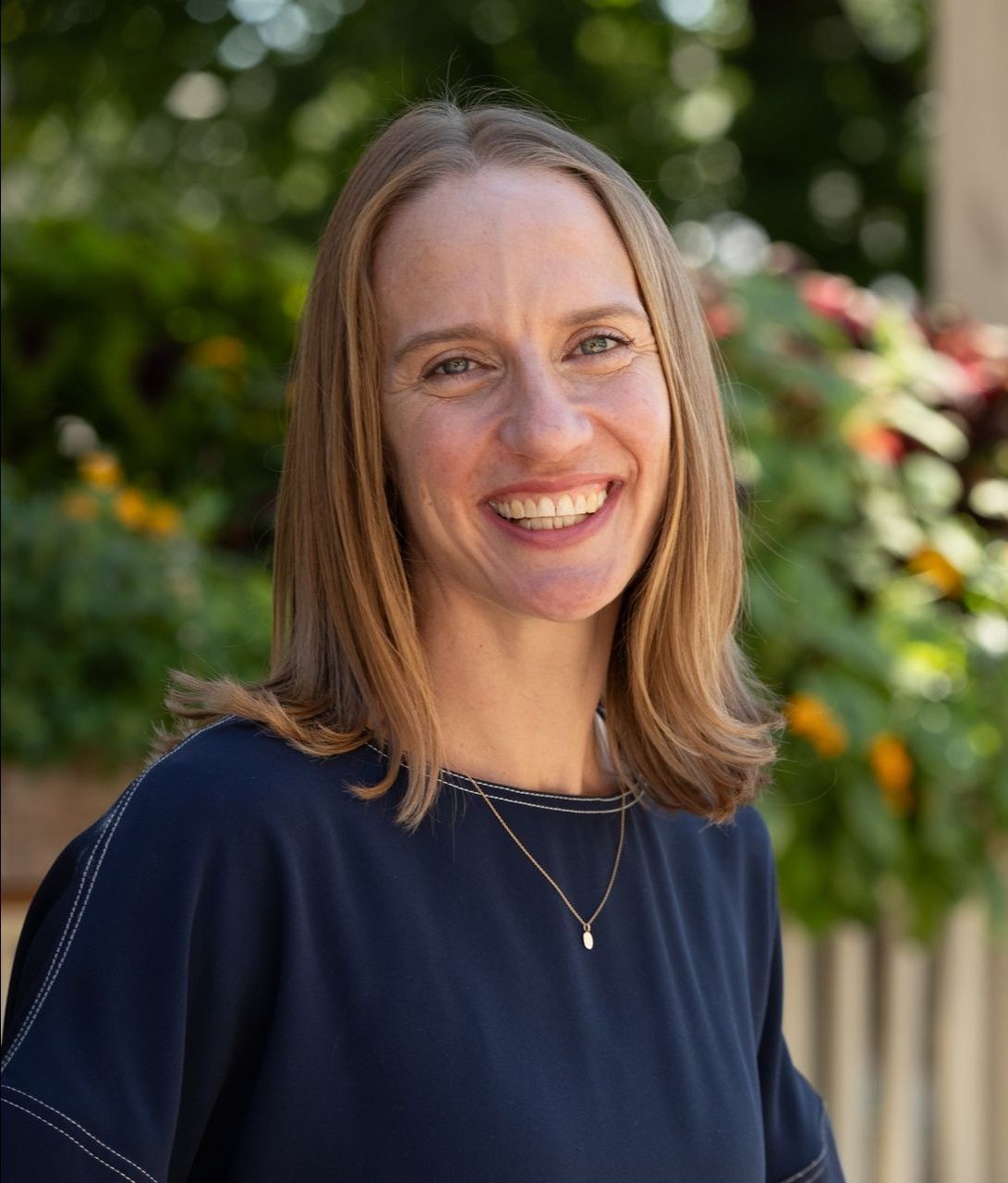 A woman in a blue shirt and necklace is smiling for the camera.