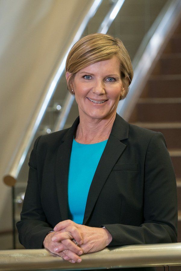 A woman in a blue shirt and black jacket is leaning on a railing.