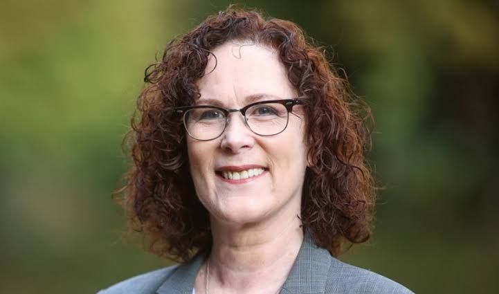 A woman with curly hair and glasses is smiling for the camera.