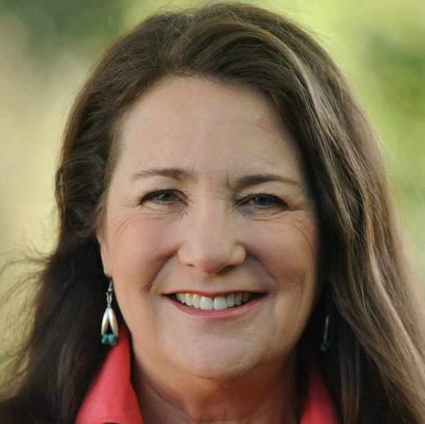 A woman wearing a red shirt and earrings smiles for the camera