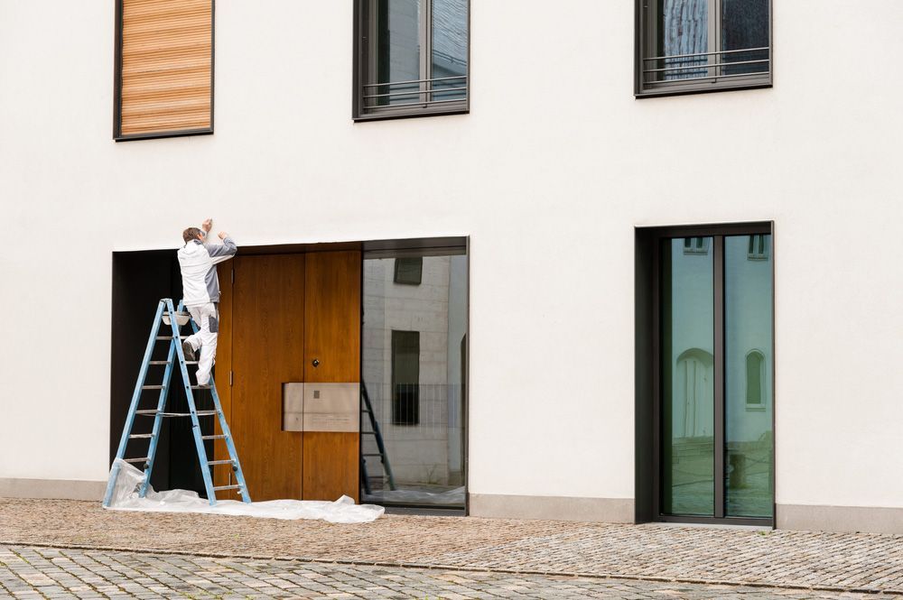Man On A Ladder Painting An Apartment Block During Exterior Renovations — Trade-Quality Building Supplies in Armidale, NSW
