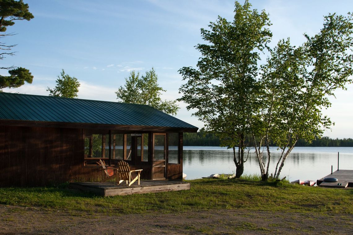 A cabin with a green roof sits next to a lake