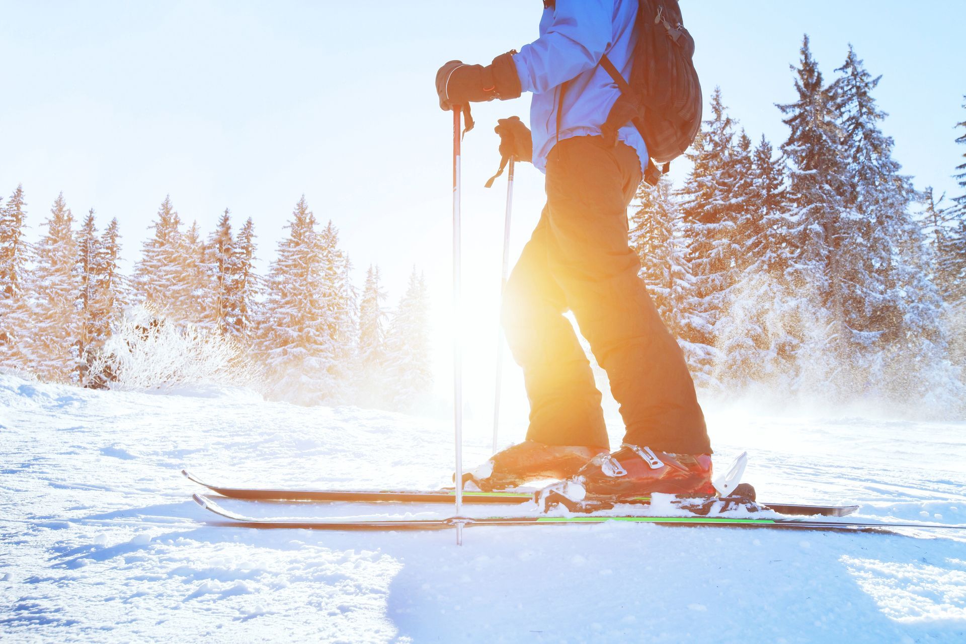 Skier on snowy slope with the sun shining, wearing blue jacket and backpack, holding poles.