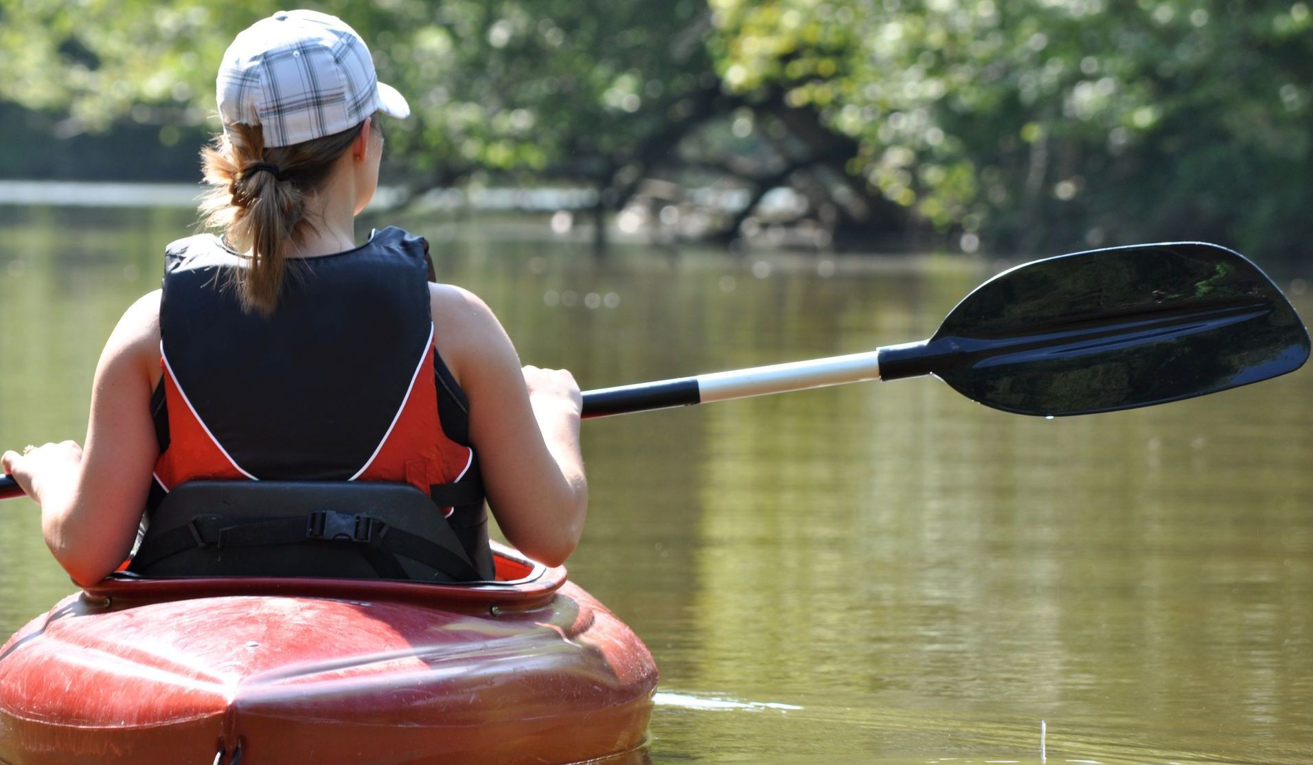 A woman is paddling a red kayak on a river.