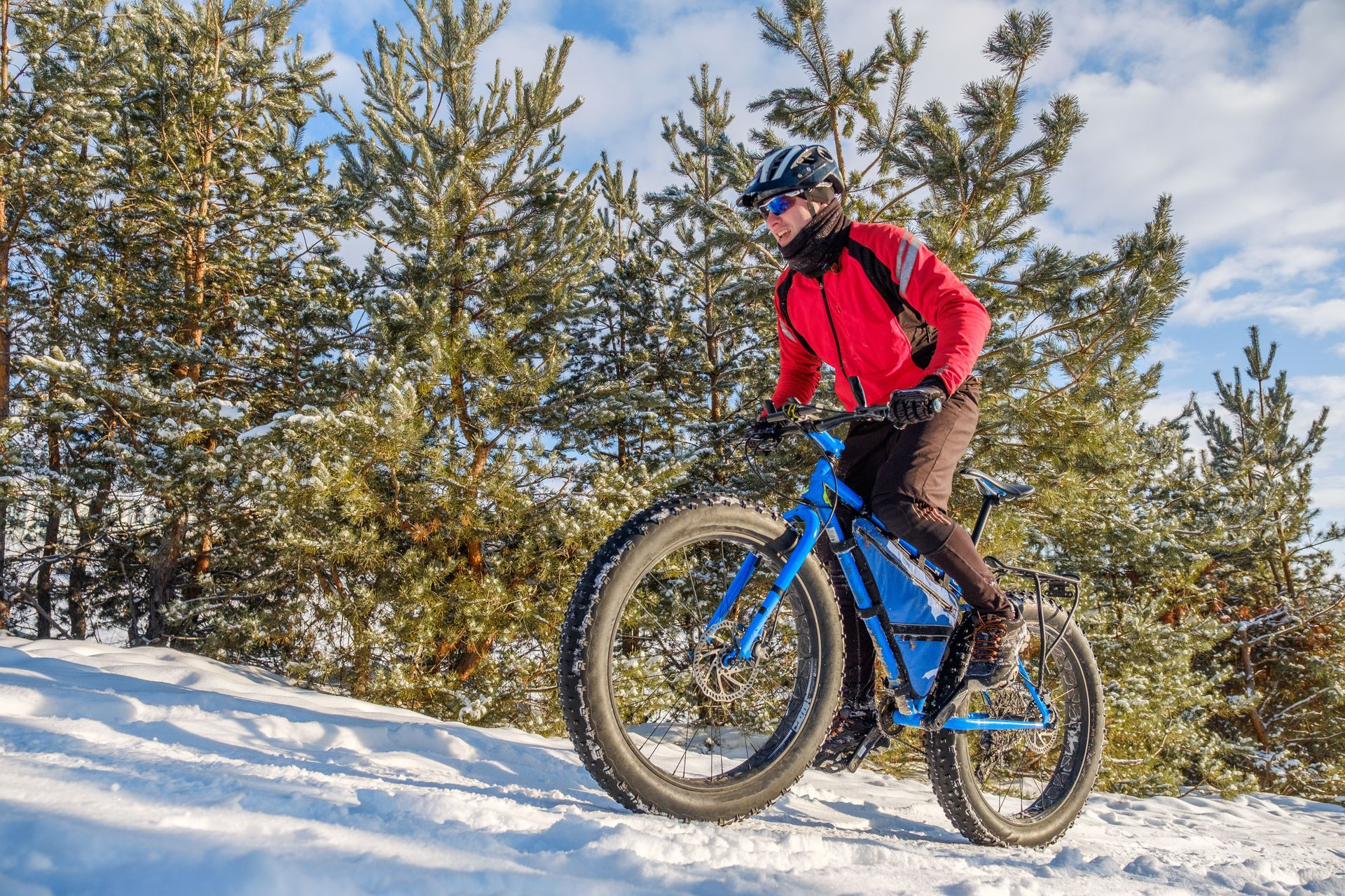 Person riding a blue fat tire bike on snow, wearing a red jacket, with trees in the background.