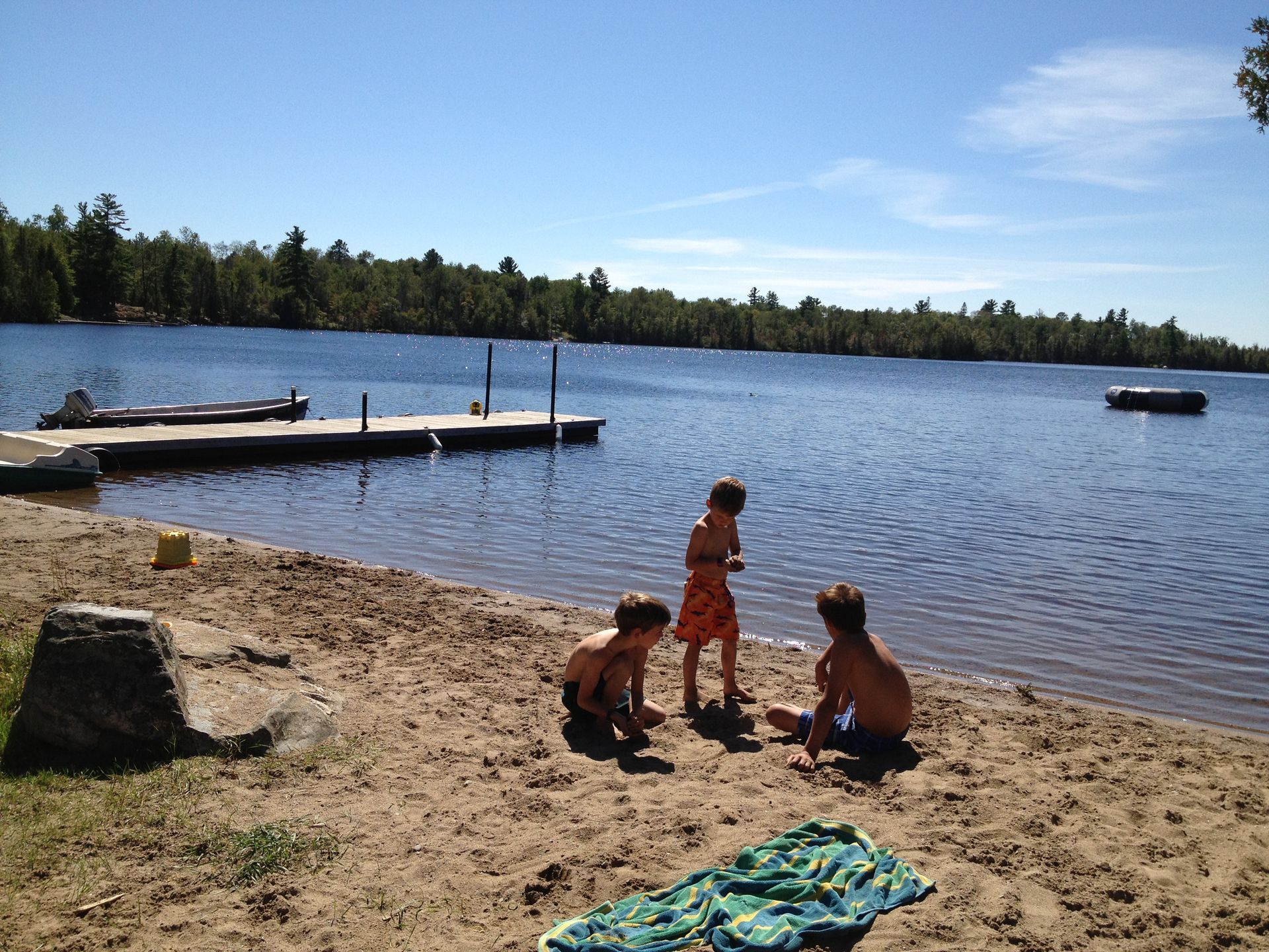 Three children are playing in the sand near a lake
