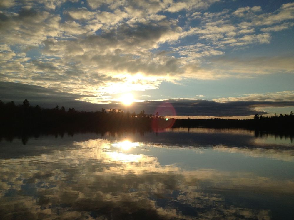 The sun is setting over a lake with clouds reflected in the water.