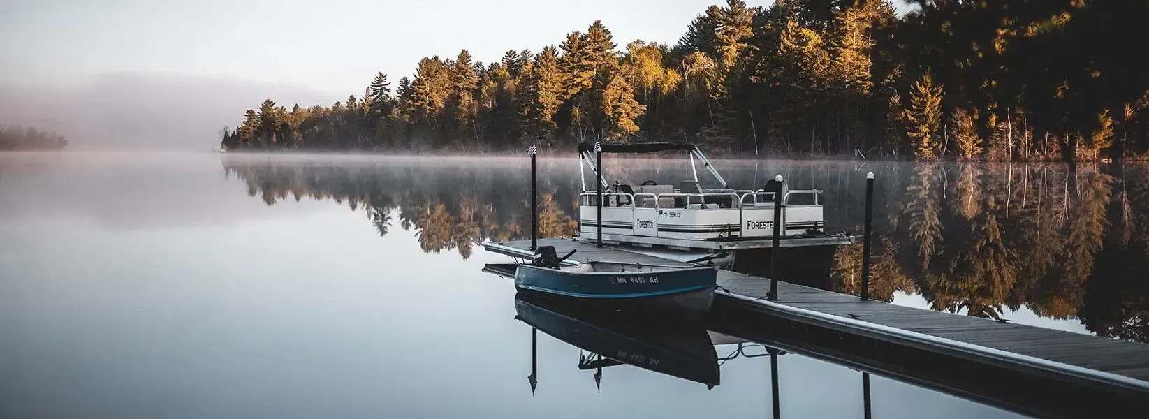 A boat is docked at a dock on a lake surrounded by trees.
