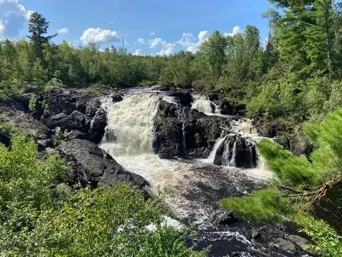 A waterfall is surrounded by trees and rocks in the middle of a forest.