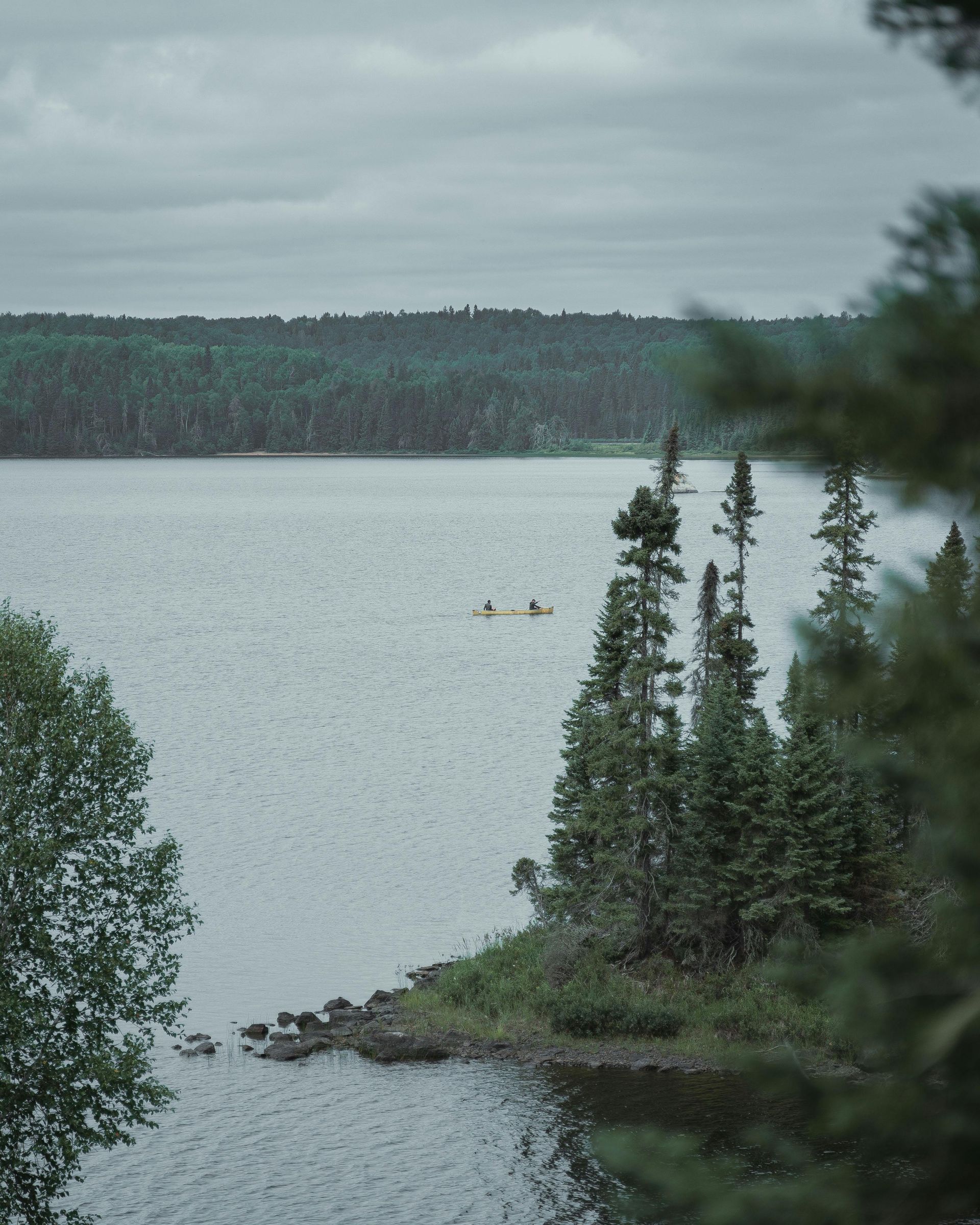 A couple of people are in a canoe on a lake surrounded by trees.