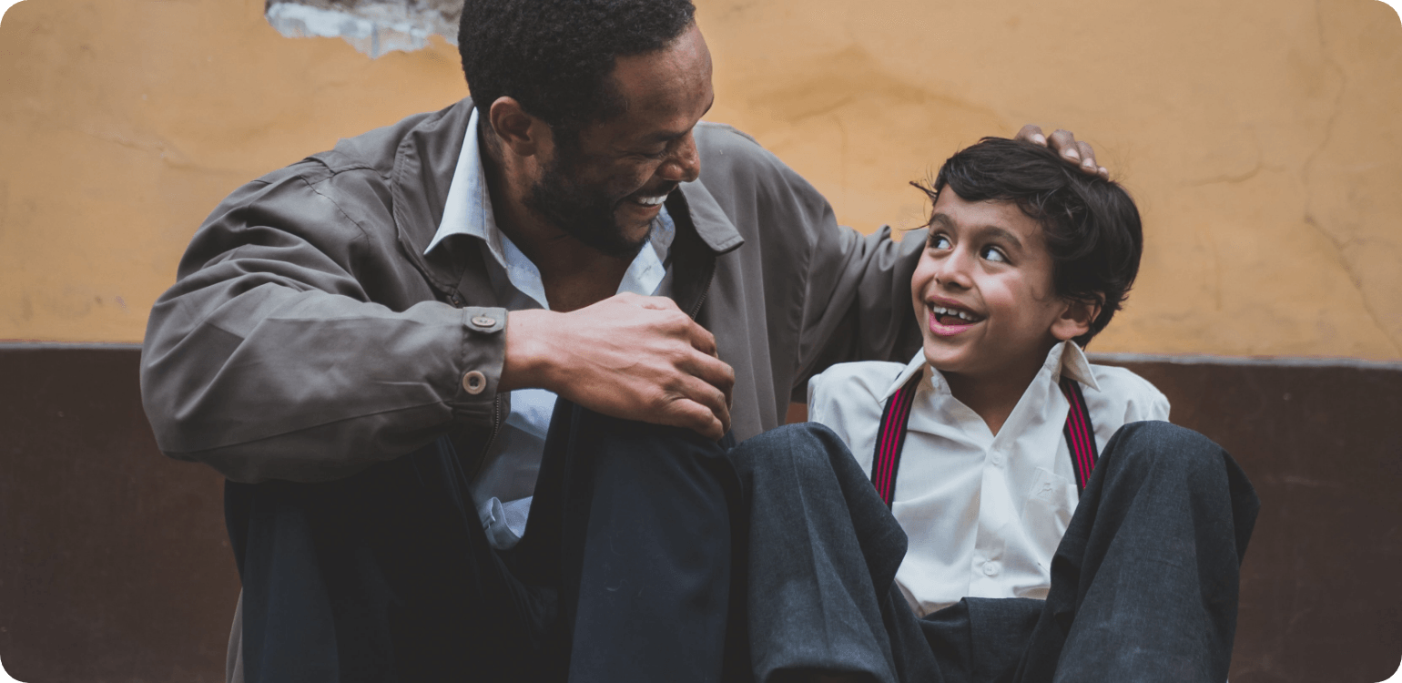 A man and a boy are sitting on the ground talking to each other.