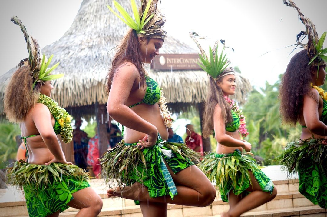 A group of women are dancing in front of a thatched hut.