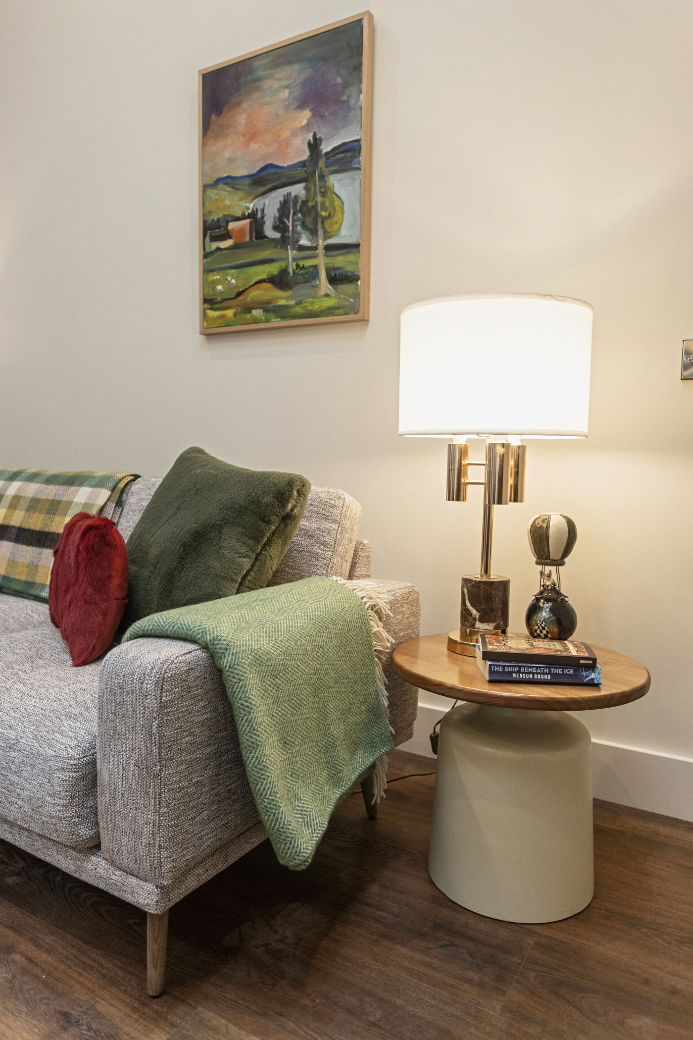 A living room with a couch , table , lamp and painting on the wall.