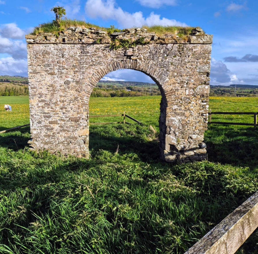 A stone archway in the middle of a grassy field