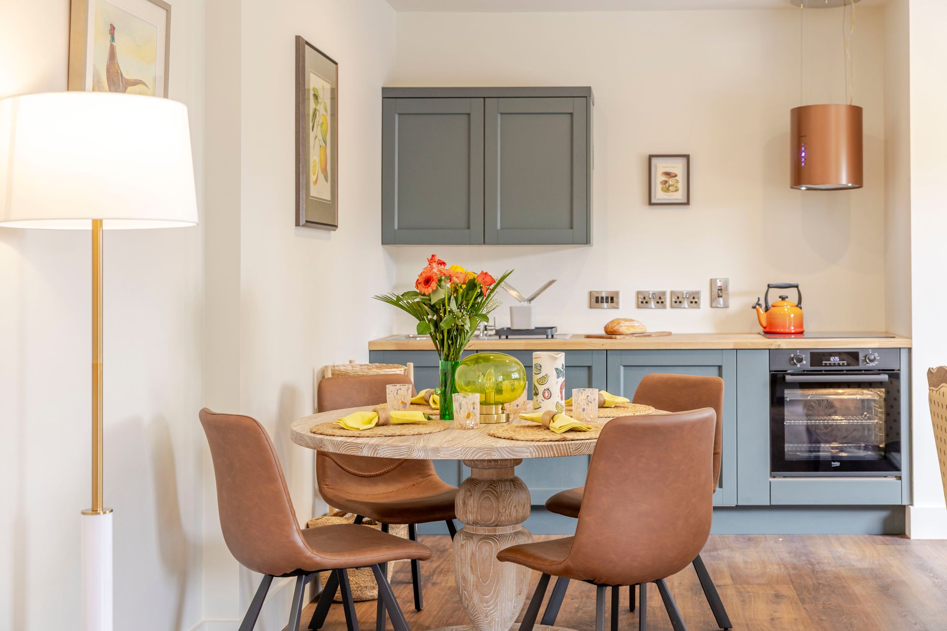 A kitchen with a table and chairs and a vase of flowers on the counter.