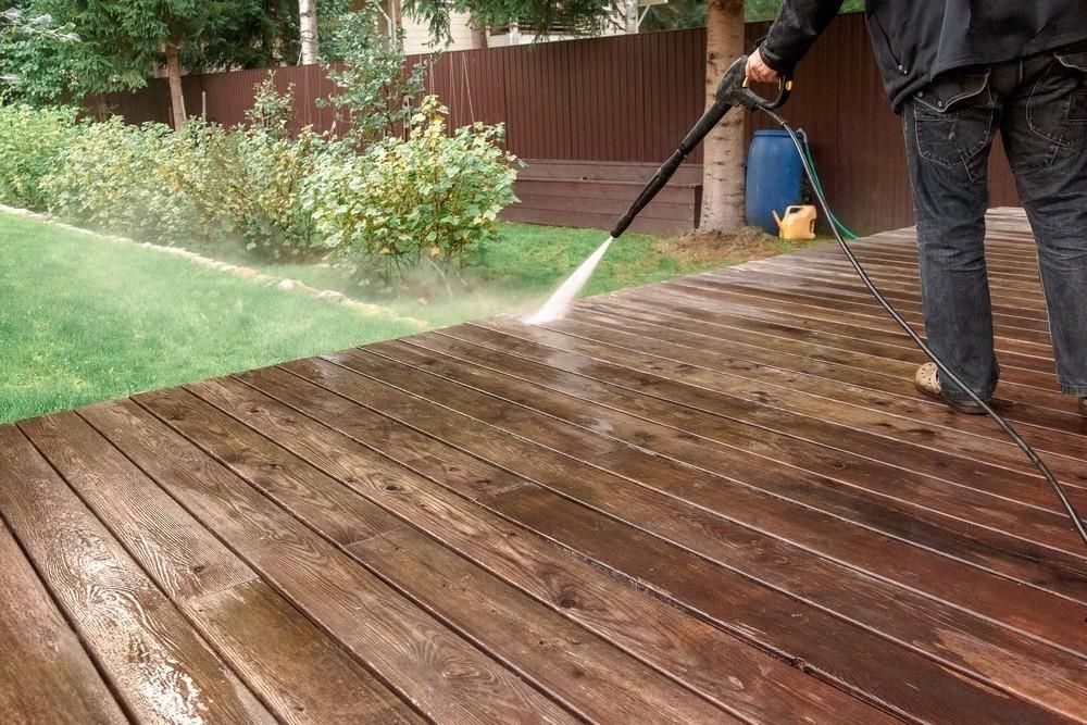 A man is using a high pressure washer to clean a wooden deck.