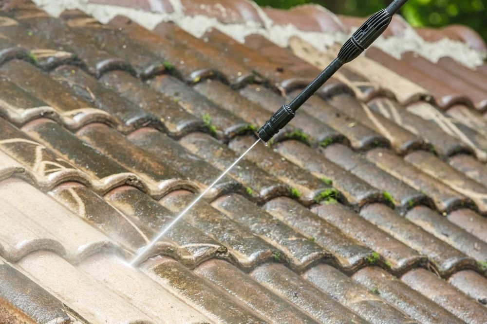 A person is cleaning a tiled roof with a high pressure washer.