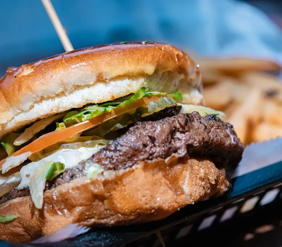 Close-up of a cheeseburger with lettuce, tomato, and pickles.