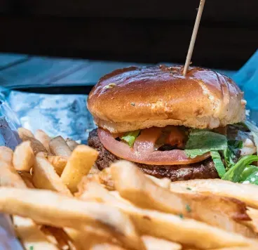 A burger and French fries served in a basket on a wooden table.