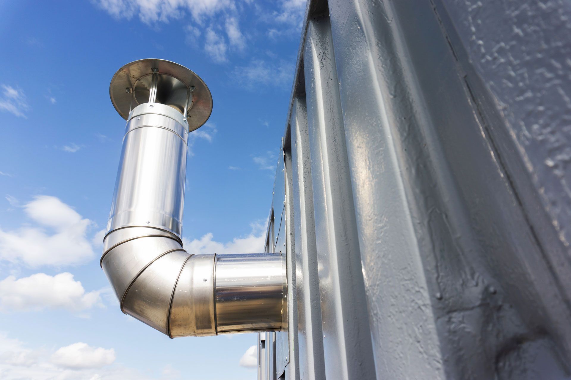 Metal chimney pipe venting from a corrugated building against a blue sky