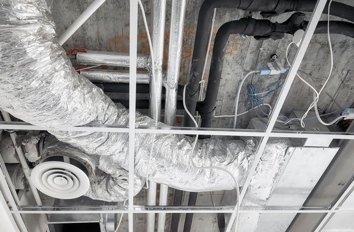 Ceiling with exposed ductwork, pipes, wires, and a round vent in an unfinished industrial space