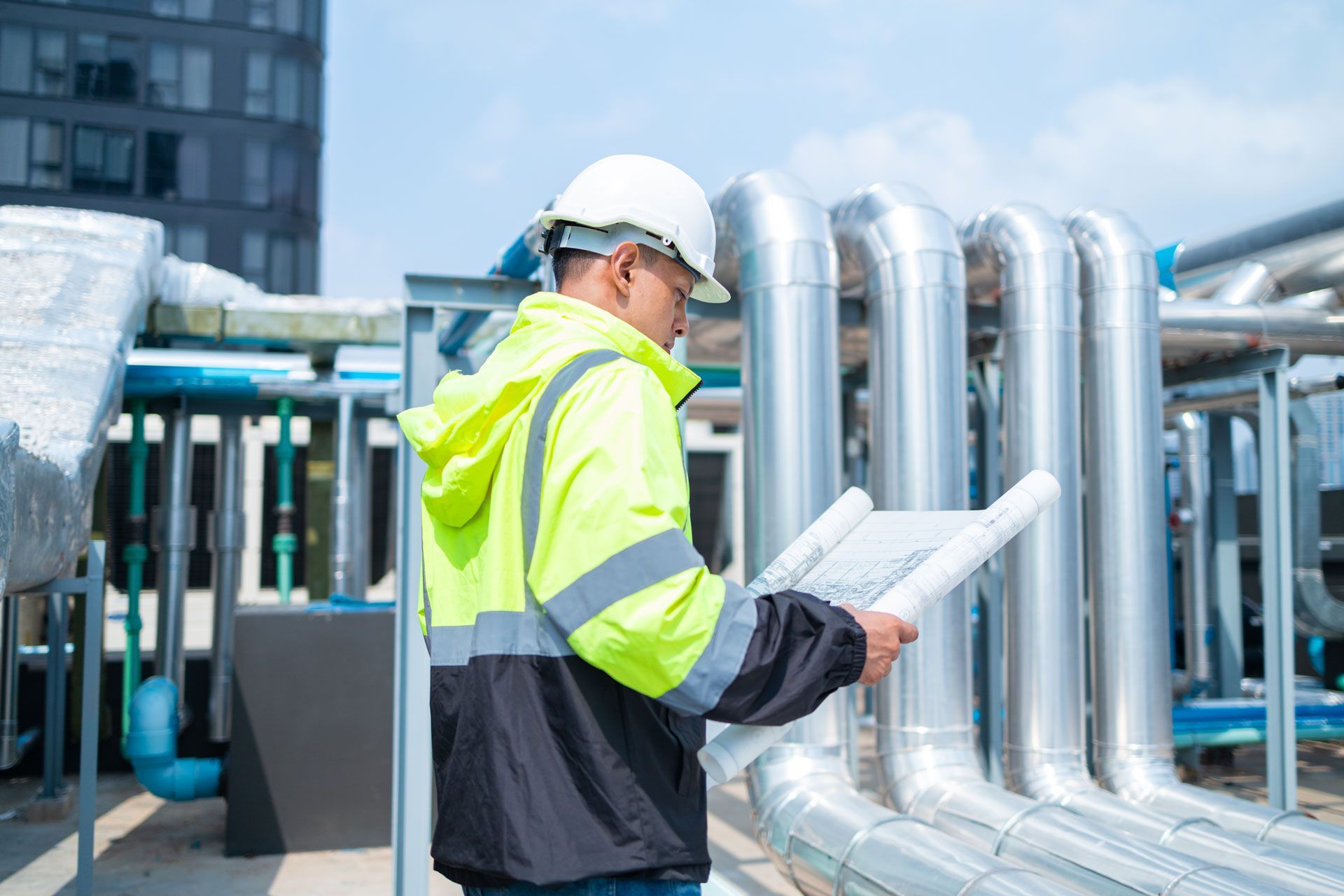 Worker in a hard hat and safety vest inspecting pipes at an industrial site