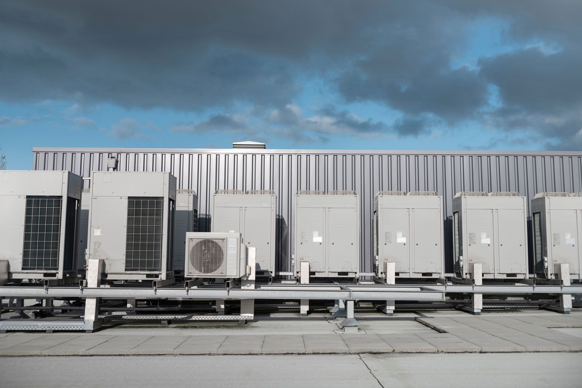 Row of industrial rooftop HVAC units against a cloudy sky