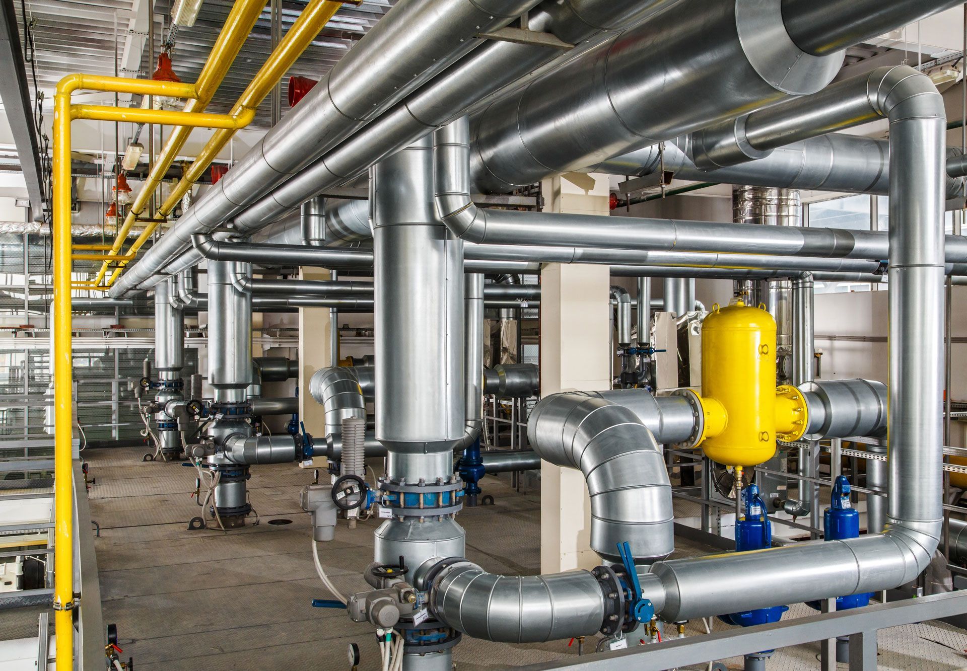 Industrial piping and valves in a plant, with silver ducts and a yellow valve assembly