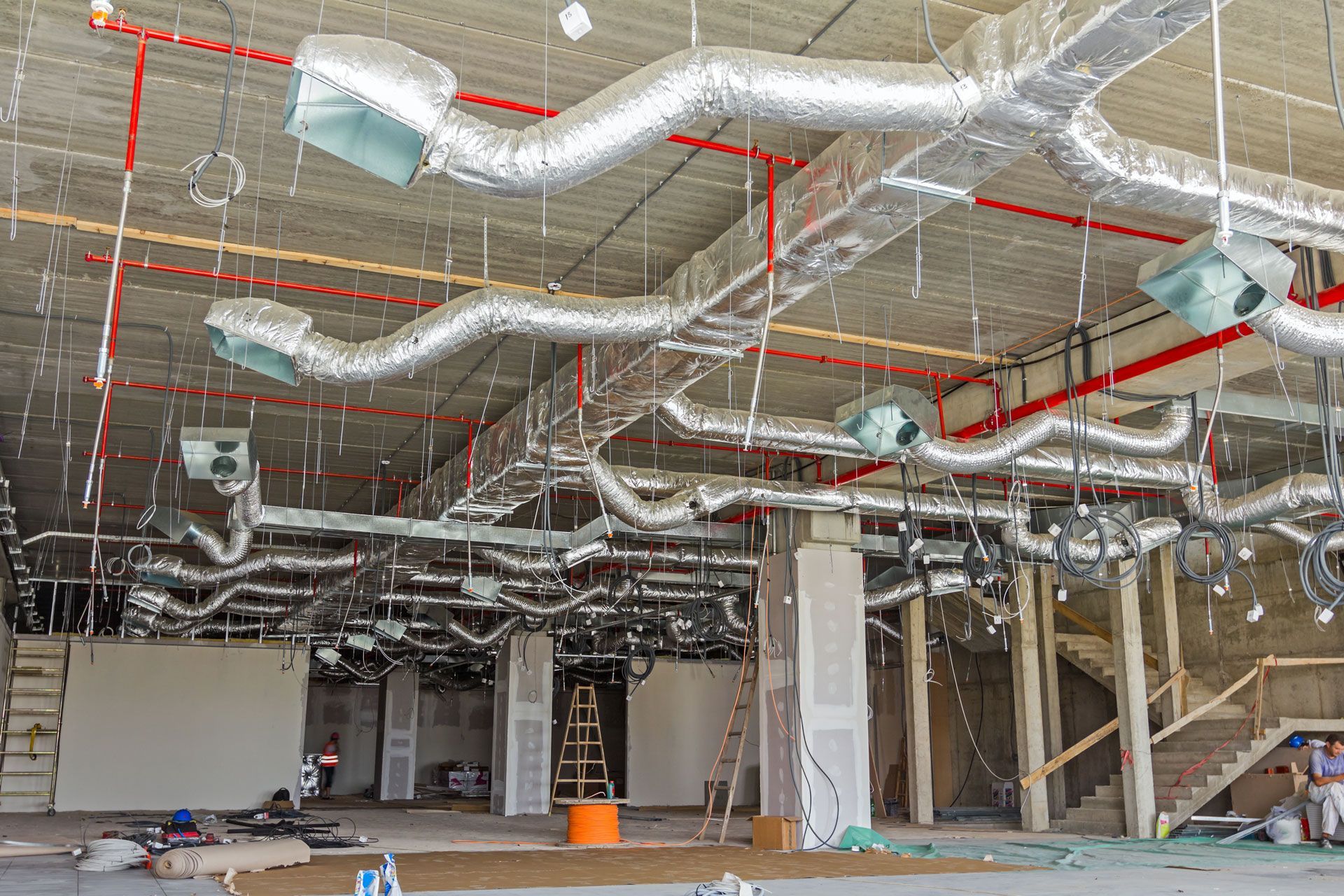 Interior construction site with exposed ductwork, red piping, and unfinished walls and ceiling
