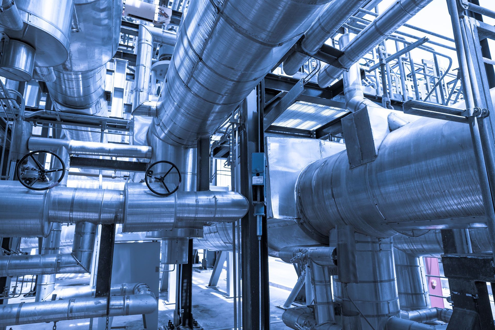 Blue-tinted industrial pipes and ducts in a factory interior