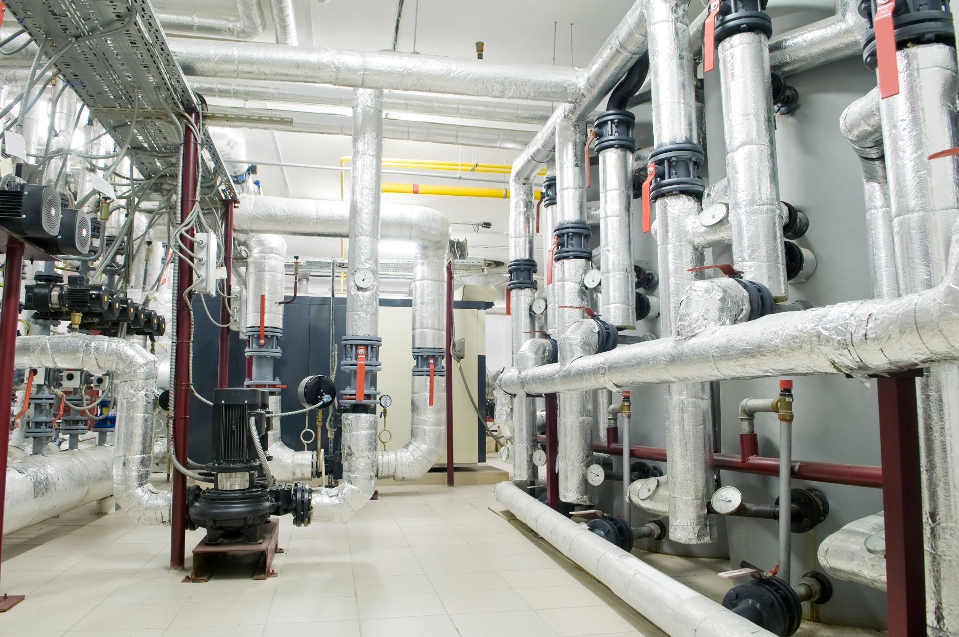 Industrial plant room with silver pipes, valves, and machinery in a bright white utility space