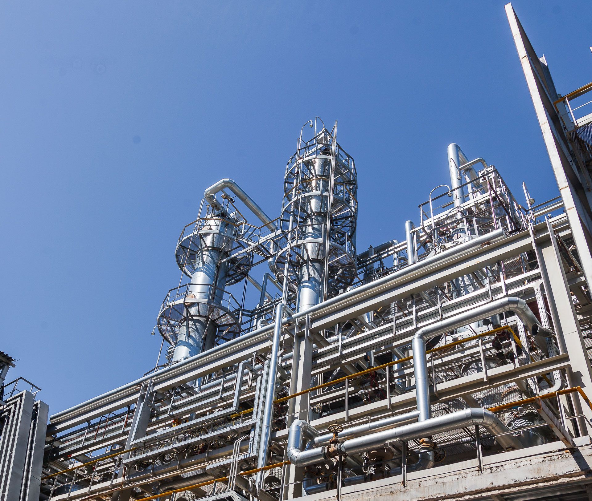 Industrial refinery with silver pipes and towers against a clear blue sky
