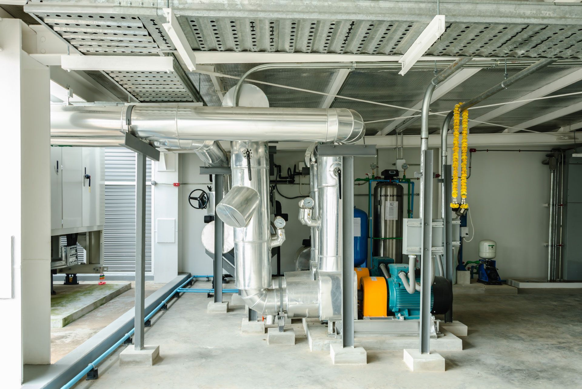 Industrial equipment and pipes in a clean mechanical room with yellow ladder and blue tank