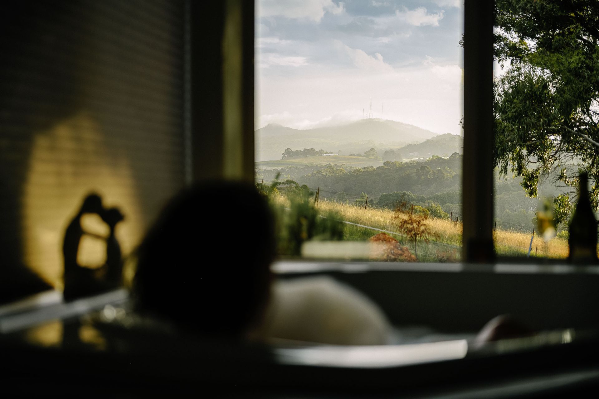 Person lounging by a window, looking out at a bright mountain landscape beyond the room — Lakeview Luxury Retreat in Canobolas, NSW