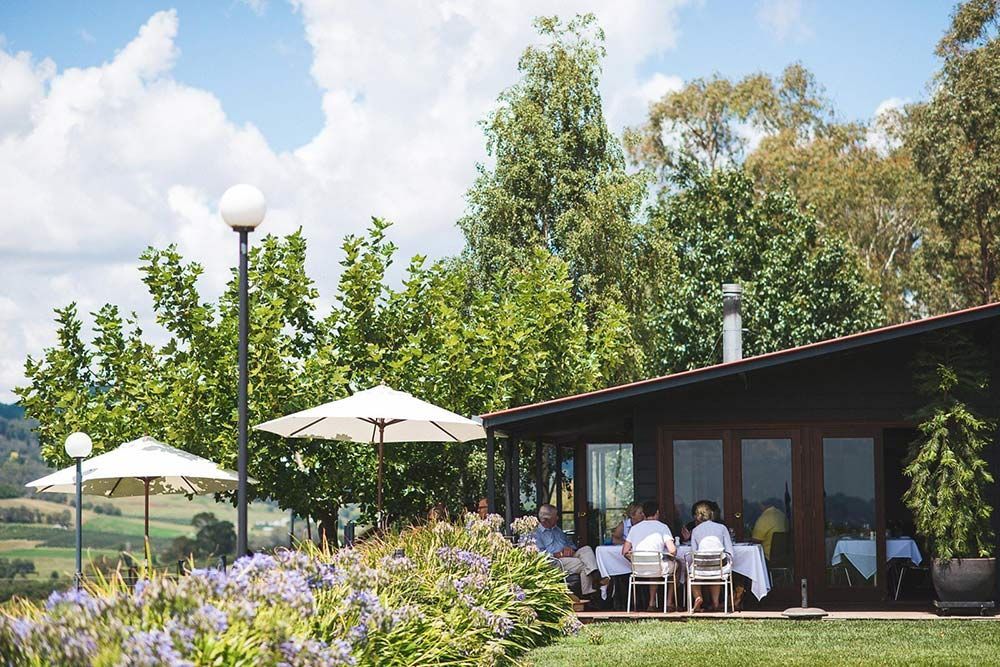 A Group of People Are Sitting at Tables Outside of a House With Umbrellas — Lakeview Luxury Retreat in Canobolas, NSW
