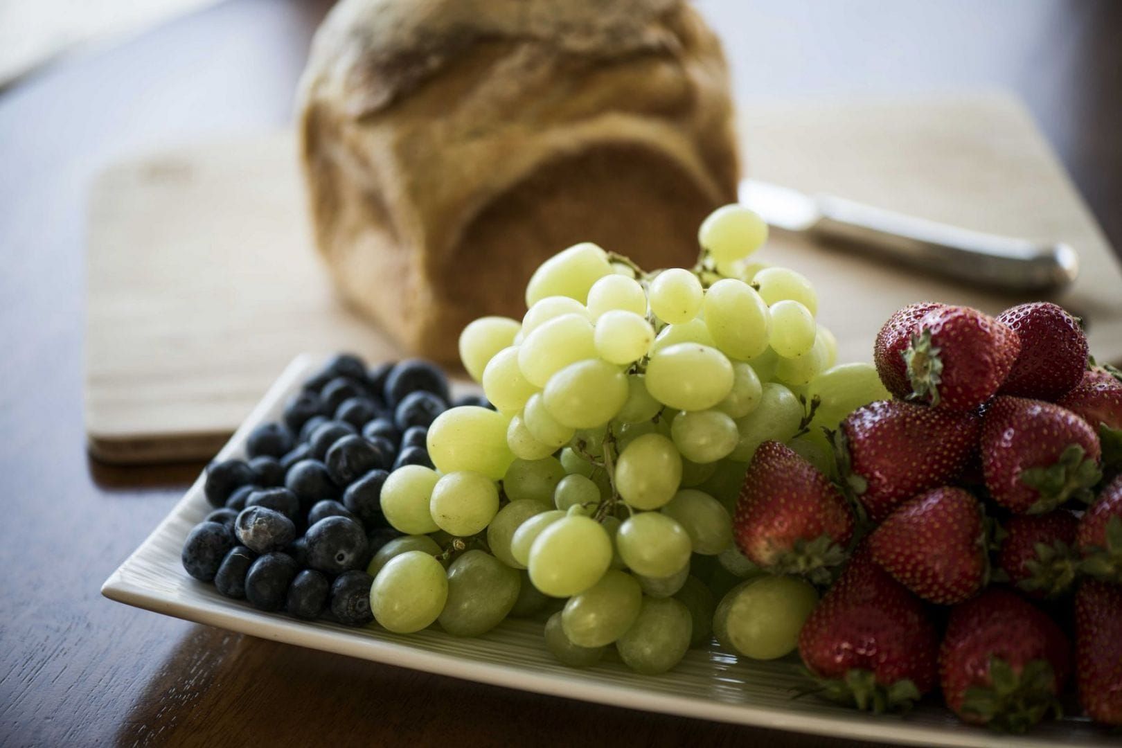 A Plate of Grapes Strawberries and Blueberries on a Table With a Loaf of Bread — Lakeview Luxury Retreat in Canobolas, NSW