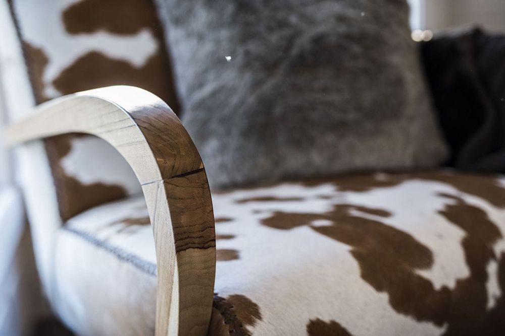 A Brown and White Cow Print Chair With a Wooden Arm Rest — Lakeview Luxury Retreat in Canobolas, NSW