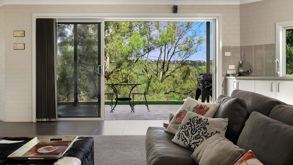 A Living Room With a Couch and a Sliding Glass Door Leading to a Deck — Lakeview Luxury Retreat in Canobolas, NSW