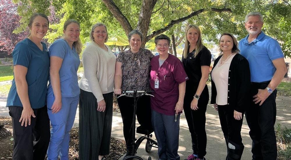 Group of people outdoors, one using a knee scooter, under a tree.