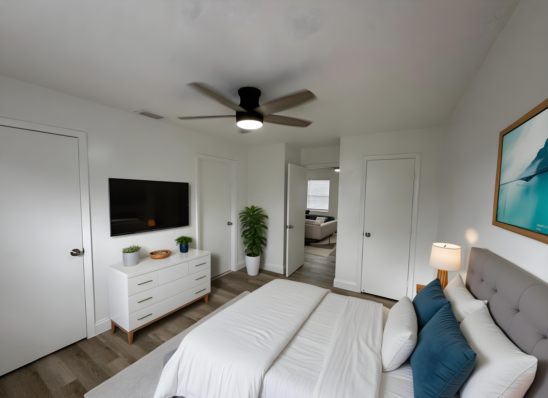 Bedroom with bed, dresser, TV, and doors. White walls and ceiling fan.