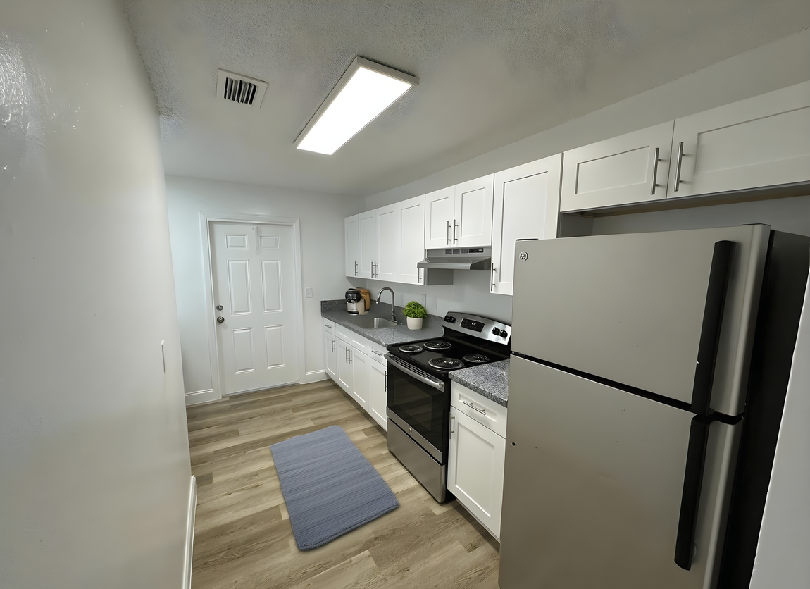 Small, white kitchen with stainless steel appliances, white cabinets, and a gray countertop.