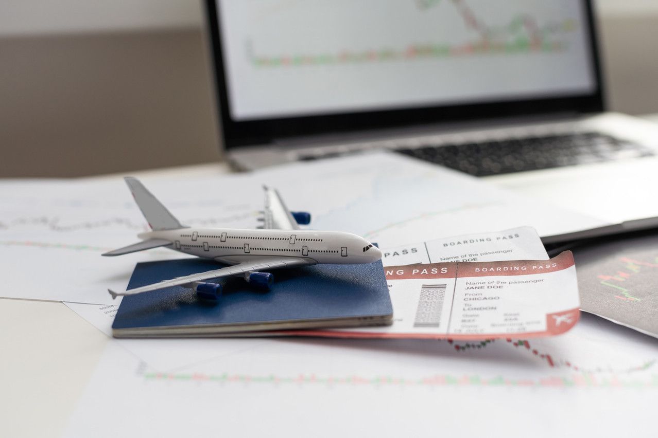 Model airplane, tickets, and passport on a desk, with laptop and charts in the background.