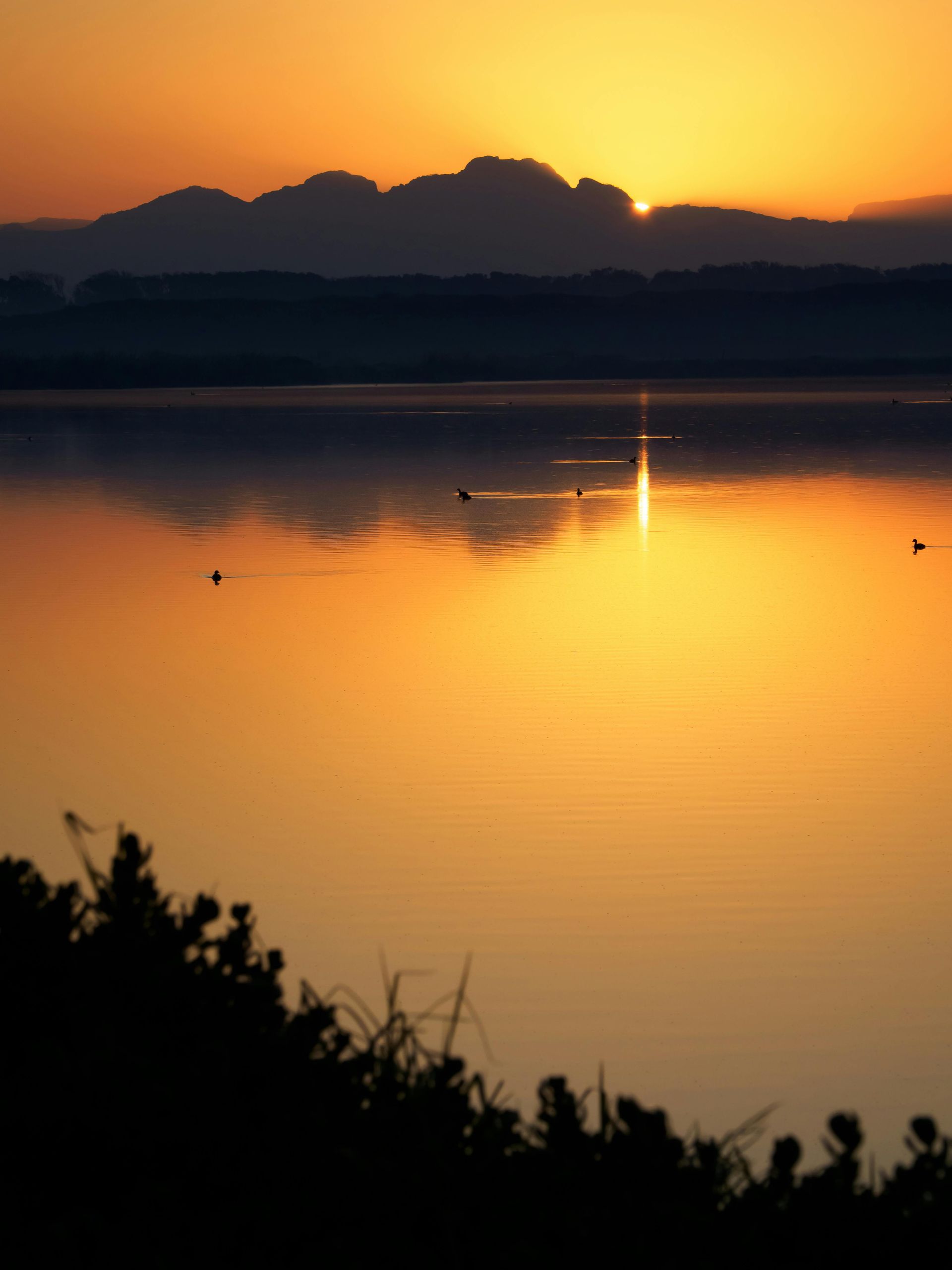Un coucher de soleil sur un lac avec des montagnes en arrière-plan