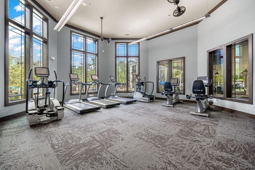 a large gym with treadmills, exercise bikes, and mirrors at Marquis on Lakeline in Cedar Park, TX.