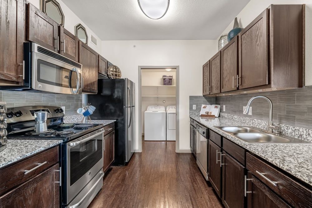 a kitchen with stainless steel appliances, granite counter tops, and wooden cabinets at Marquis on Lakeline in Cedar Park, TX.