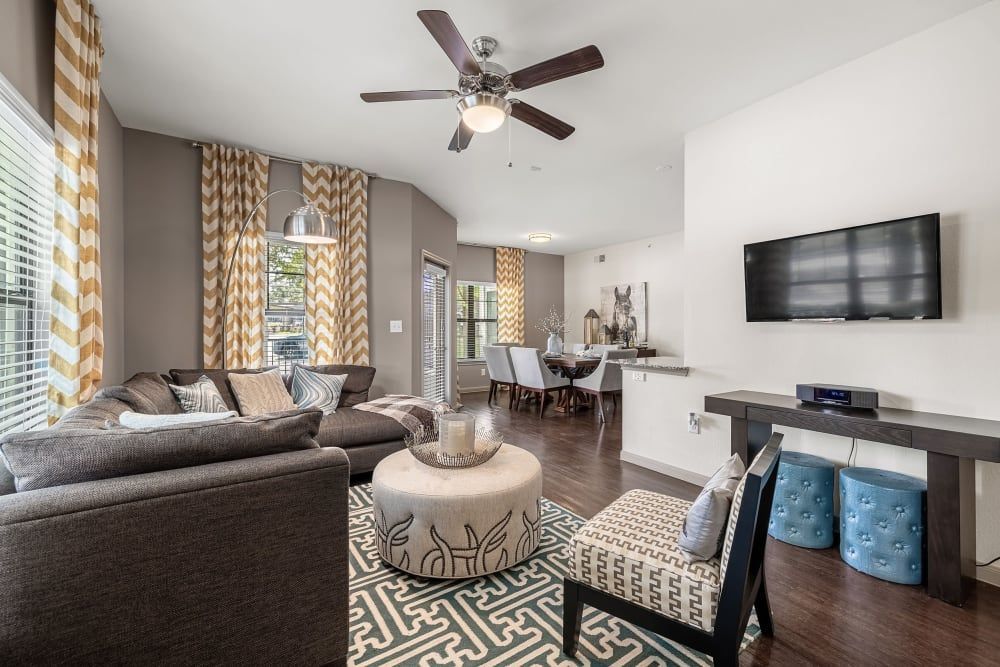 a living room with a couch, chairs, ottoman, television, and ceiling fan at Marquis on Lakeline in Cedar Park, TX.